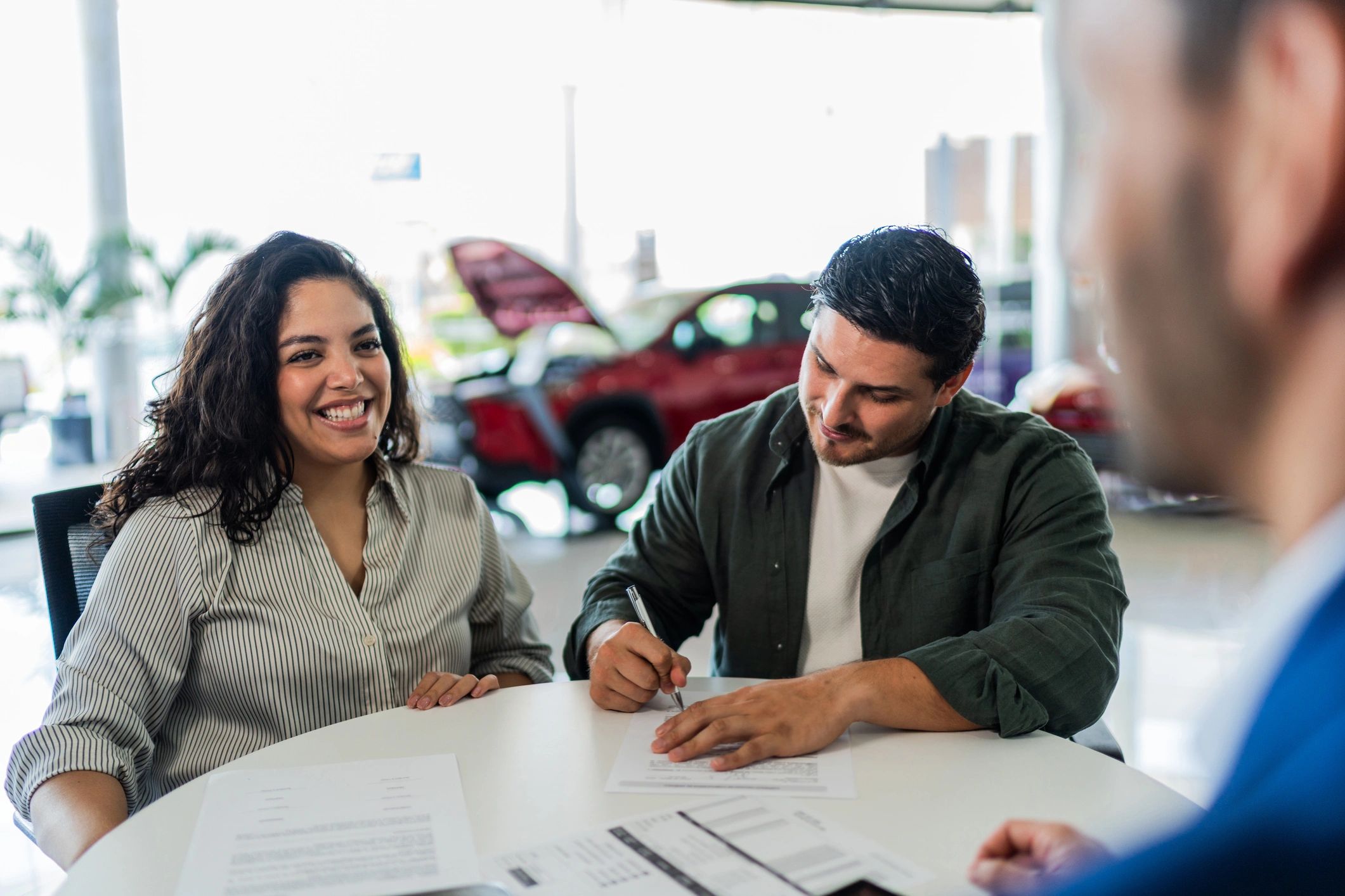 Couple working with a sales professional at a car dealership desk